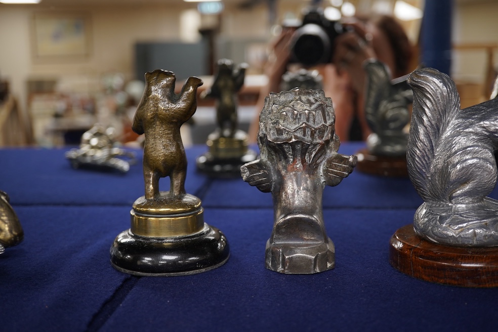 Seven chrome, brass and aluminium car mascots, etc. including an unusual and comical aluminium car mascot in the form of a squirrel holding a nut, together with a standing bear, an Art Deco winged head, a ram, a running